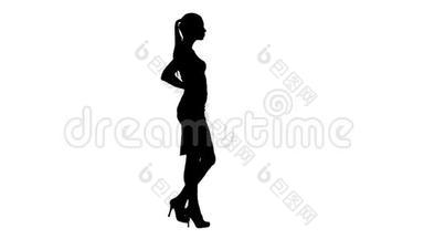 剪影美丽的年轻女子穿着优雅的服装行走，双手抱着臀部。